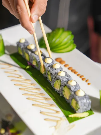 A chef uses chopsticks to perfectly place our charcoal-infused avocado sushi rolls. The precision and care taken in creating each piece is a hallmark of our sushi program.