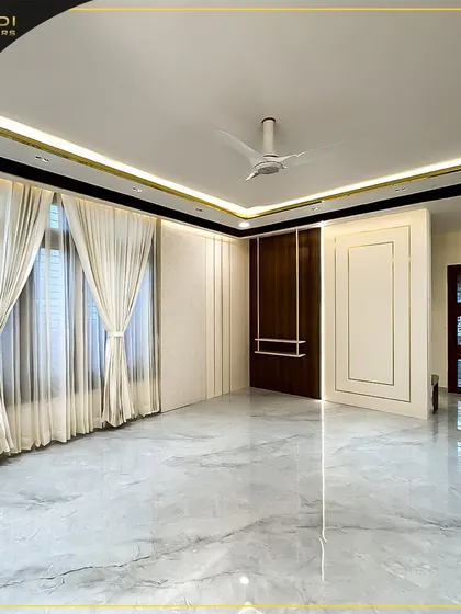 An empty, spacious room with elegant full-length curtains, showcasing the potential for a grand living area. The marble flooring and cove lighting in the ceiling set a luxurious foundation.