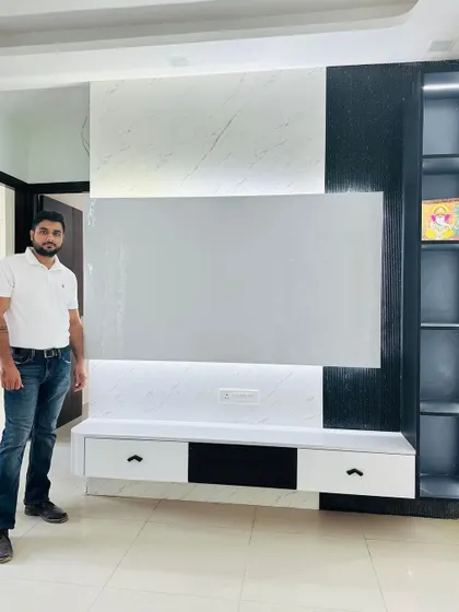 Standing next to a newly installed TV unit. This design features a clean, modern aesthetic with a black and white theme, a backlit panel, and open shelving on the side for display.