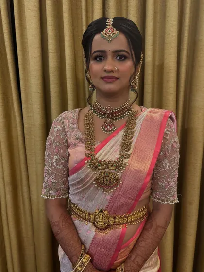 A portrait of a bride in a classic pink and white saree, her hair in a neat updo that highlights her beautiful jewellery.