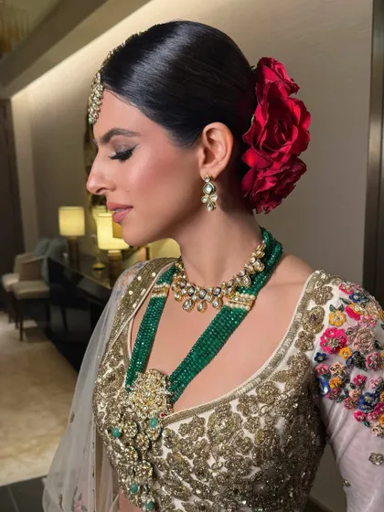 A side profile of the bride, her sleek bun adorned with a large red rose, perfectly complementing her emerald jewelry.