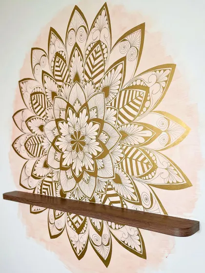 A full view of the gold leaf mandala on a soft blush watercolor background. It sits perfectly above a wooden shelf, creating a beautiful focal point.