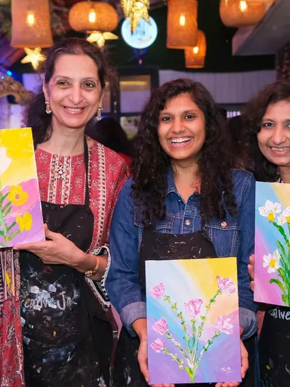 Three women smile as they display their beautiful floral paintings, each with its own unique color palette, created during a fun group event.