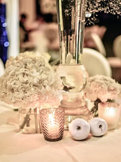 The warm candlelight at night transforms the simple elegance of the white apples and hydrangea arrangements into a cozy and romantic scene.