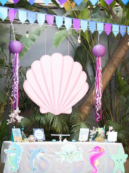 I transform your space into a different world. This under-the-sea themed party setup features a beautiful dessert table with a giant seashell backdrop, hanging jellyfish lanterns, and ocean-themed cutouts to create an immersive experience.
