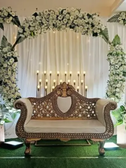 A full stage view of a half-saree ceremony at Thanisandra. The decor is clean and elegant, with a white floral arch, white drapes, and a beautiful golden sofa.