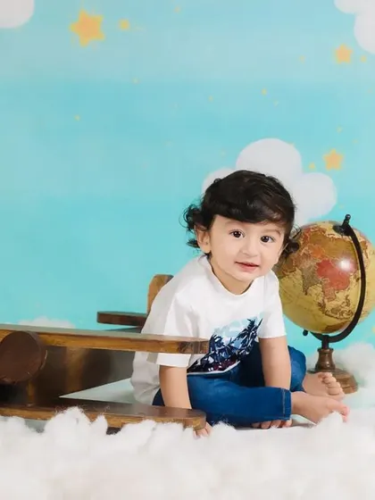 A toddler sits on a toy airplane, looking ready for an adventure among the clouds.