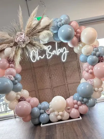 A unique take on the circular balloon backdrop for an "Oh Baby" shower. The design uses a rattan screen and a mix of blue, pink, and cream balloons, perfect for a gender-neutral or reveal party.