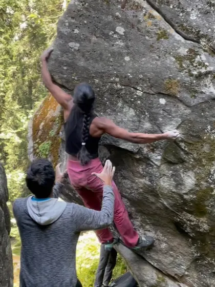 This photo captures the strength and balance required for bouldering, as a climber reaches for a hold with her spotter providing safety and confidence from below.