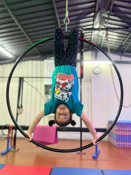 Fearless in the face of a challenge. This little one hangs upside down on the aerial hoop with a huge smile, showing that fun and fitness go hand in hand.