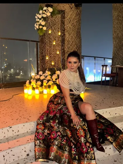 A guest posing at a rooftop party we styled. The decor features candlelit corners and floral arrangements, with the city lights providing a stunning background.