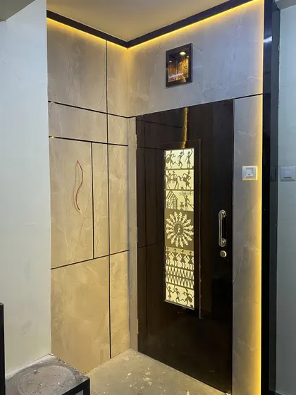 This entrance design features a door with a backlit panel showcasing traditional Warli art. The surrounding stone-finish wall panels are also backlit for a dramatic effect.