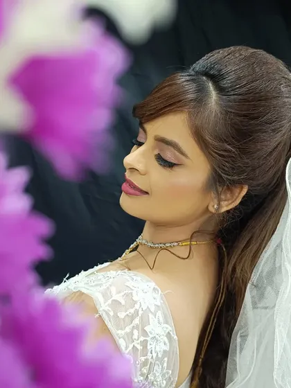 A side profile of my beautiful Catholic bride, framed by flowers. The makeup is soft and romantic, with a focus on luminous skin and a gentle pink lip, complementing her delicate lace dress.