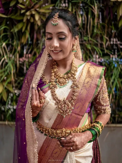 A detailed portrait focusing on the bride's magnificent jewelry and the rich textures of her saree. Her gentle smile reflects the happiness of her special day.