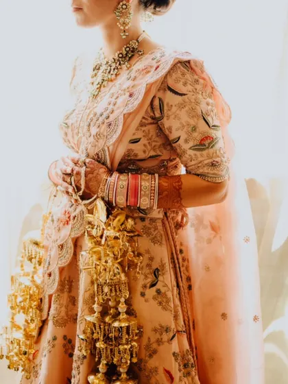 A detailed shot of the bride's pastel lehenga and her golden kaleeras, capturing the intricate beauty of her bridal attire.