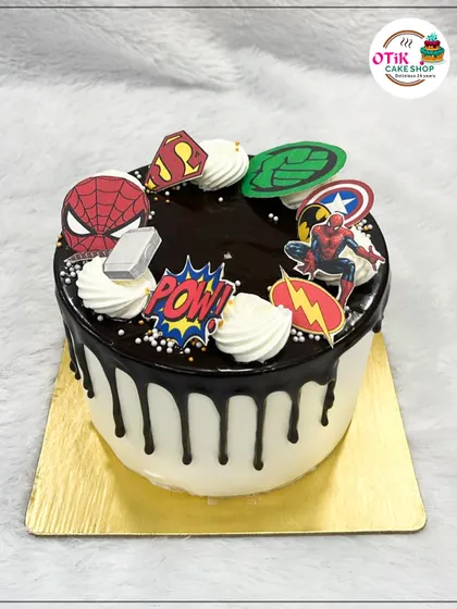 A fun superhero-themed drip cake. The chocolate ganache drips over a white base, and the cake is decorated with edible logos of all the favorite heroes.