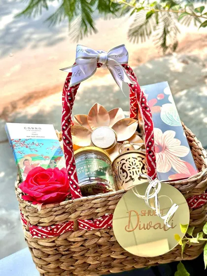 A festive Diwali basket with a red and white theme, featuring a lotus diya, a lantern, and a "Shubh Diwali" acrylic tag.