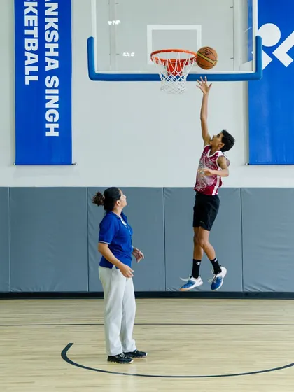 A young player practicing his layup form with a coach watching on.
