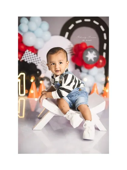 A cool little dude celebrating his first birthday. The race car theme with checkered flags and balloons sets a fun and energetic mood.