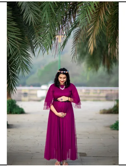 A full-length portrait of a mom-to-be in a lovely purple gown, framed by palm leaves.