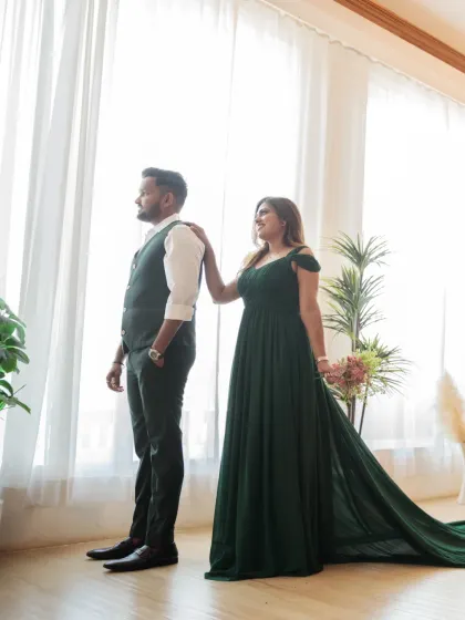 A quiet, reflective moment by the window. The bride's hand on the groom's shoulder and their shared gaze outwards create a feeling of partnership and shared dreams.