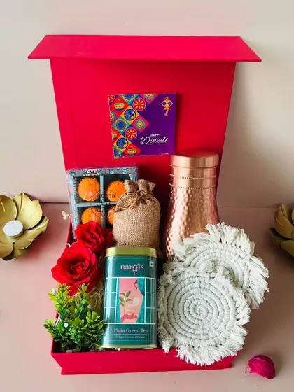 This premium hamper in a red magnetic box includes a copper bottle, macrame coasters, green tea, and laddoo candles.