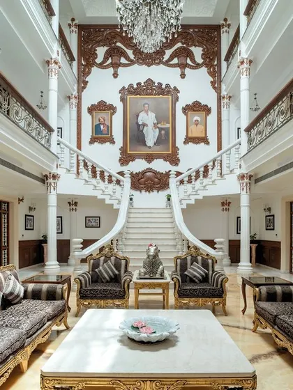 The heart of "The Palace Promised," this triple-height living room features ornate furniture, gilded accents, and a grand staircase backdrop, creating a space that is both magnificent and welcoming.