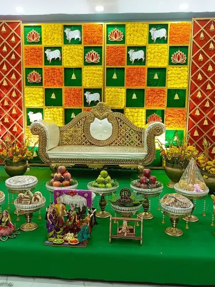 A full view of a traditional Seemantham stage, complete with a floral checkerboard backdrop and an elaborate display of offerings. The setup includes traditional dolls and cow motifs for a truly authentic feel.