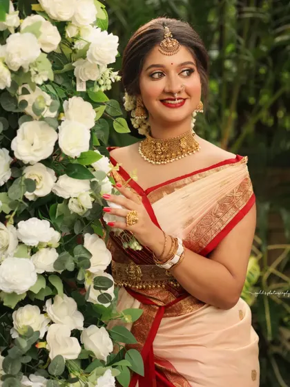 Portraits from a makeup shoot, showcasing a model in a classic red and cream saree. The images highlight the flawless makeup and traditional styling in a beautiful garden setting.
