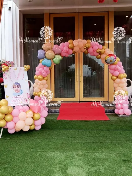A charming balloon arch in pink and gold creates a welcoming entrance for a butterfly-themed first birthday party, complete with a personalized welcome sign.