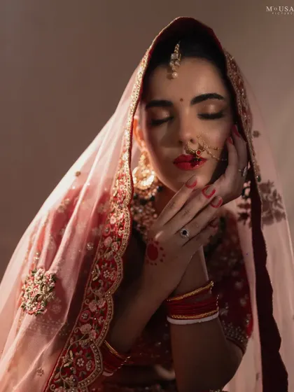 An artistic bridal portrait with eyes closed, hands gently framing the face. The warm lighting and traditional alta on her hands create a serene and soulful image.