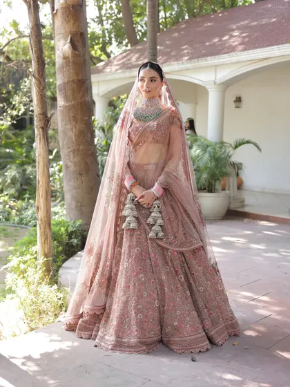 A full-length portrait of the bride in her stunning dusty rose Sabyasachi lehenga. The double dupatta draping and soft, romantic makeup create a look of pure elegance for her daytime ceremony.