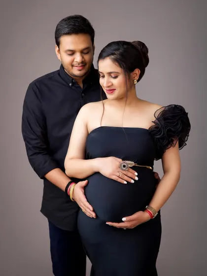 An intimate and loving portrait of the couple. The husband's hands gently cradle the baby bump, a beautiful gesture of connection and protection.