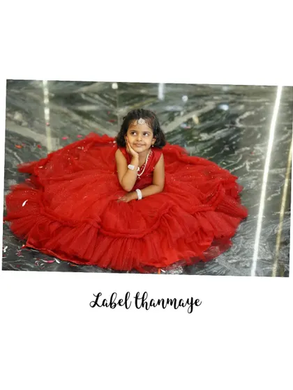 A little girl looking thoughtful in her red crop top and lehenga set. The skirt is made of layers of red tulle.