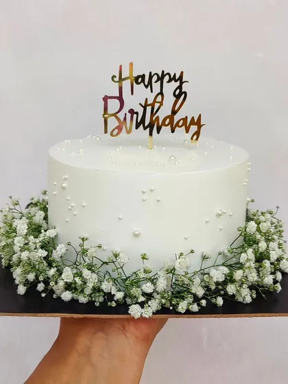 The beauty of simplicity. This pure white cake is decorated with delicate pearl sprinkles and a wreath of fresh baby's breath at the base.