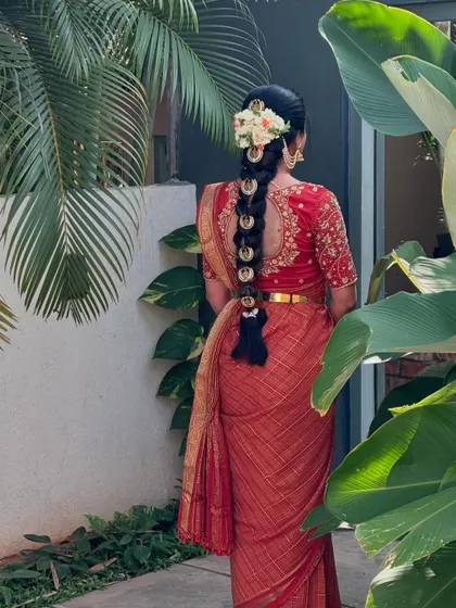 A long, traditional braid decorated with golden billai discs and fresh white flowers, styled for a client in a red saree.