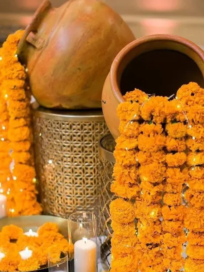A close-up of a traditional decor element for a home function. Marigold garlands with embedded fairy lights spill out of earthen pots, creating a warm and festive glow.