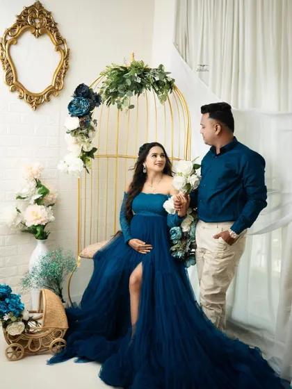 The couple stands together in the floral setup, sharing a look of love. The coordinating colors of their outfits create a harmonious and elegant portrait.