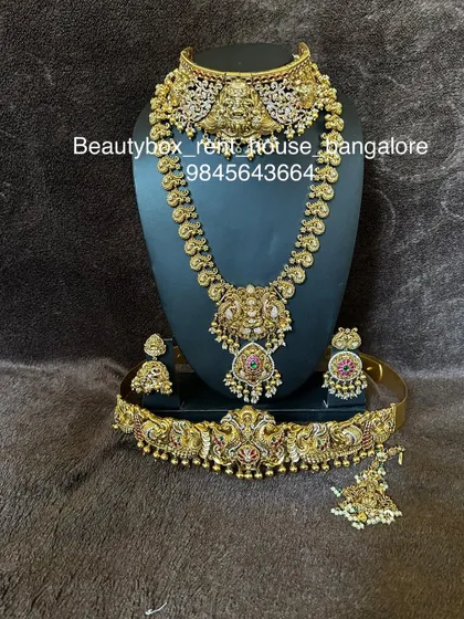 This rental set features a unique combination of a temple choker and a kasu-style long necklace, paired with a peacock-motif vaddanam.