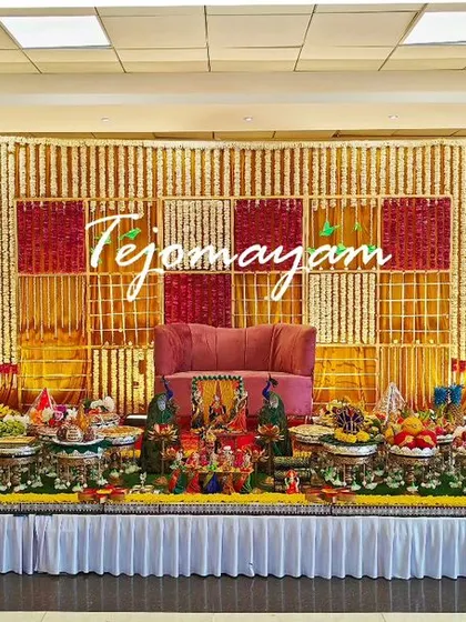 A classic baby shower stage with a red and yellow marigold checkerboard backdrop, flanked by tall brass lamps.