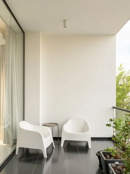 The balcony offers a comfortable outdoor space with views of the surrounding greenery. The simple glass railing ensures an unobstructed connection to the outdoors.