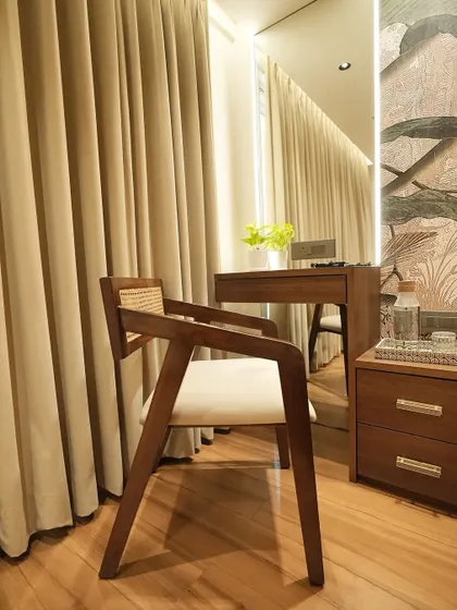 Another angle of the elegant wooden and rattan chair, placed next to a vanity. Its timeless design complements the warm wooden floors and soft curtains, adding to the room's serene atmosphere.