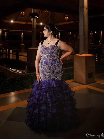 A custom-designed sangeet gown in a deep purple. The bodice is heavily embellished with crystals, and the skirt features dramatic ruffles.