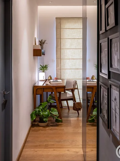A corridor lined with family photos leads to a quiet study nook, demonstrating how we design homes that can be personalized over time. A large mirror at the end of the passage creates an illusion of extended space.