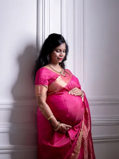 A graceful solo portrait of a mom-to-be in a vibrant pink saree, captured against a clean, white wall in our studio for a modern look.
