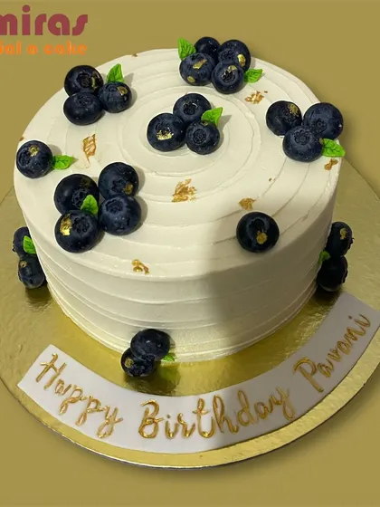 A fresh and elegant blueberry cake. The white buttercream is topped with clusters of fresh blueberries and flecks of gold leaf for a simple yet sophisticated birthday design.