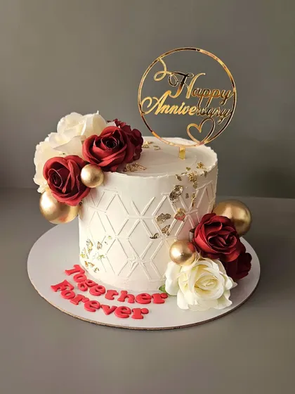 A pretty anniversary cake in red and white. This butterscotch cake is decorated with a geometric stencil pattern, red and white roses, and gold accents.