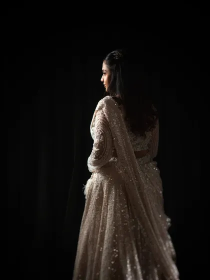 A study in light and shadow. This portrait uses a single light source to sculpt the bride's form and the beautiful texture of her lehenga, creating a sense of mystery and elegance.