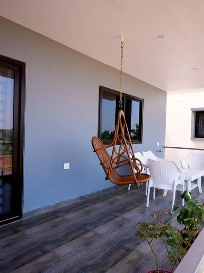 A simple and serene balcony with a wooden swing, white outdoor furniture, and a wood-plank style floor, offering a peaceful spot to relax.