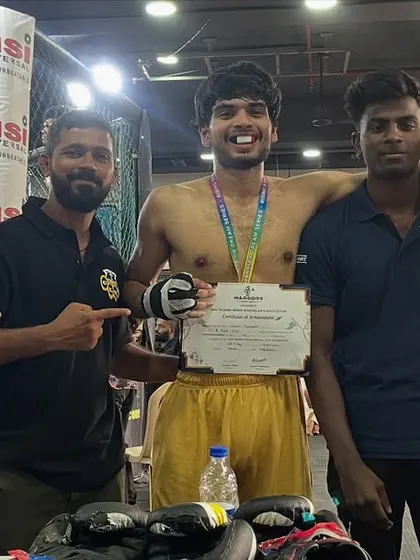 A fighter celebrating his first combat sports win at a WDS K1 event, surrounded by his coaches and teammates.